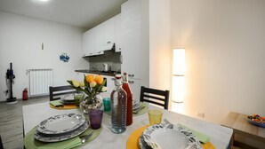 A dining area with a table set for two, a kitchen in the background, and a wall-mounted light fixture. - Cozy apartment in Carro with WiFi (Carro)