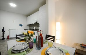 Ein Essbereich mit Tisch für zwei Personen, eine Küche im Hintergrund und einer Wandleuchte.