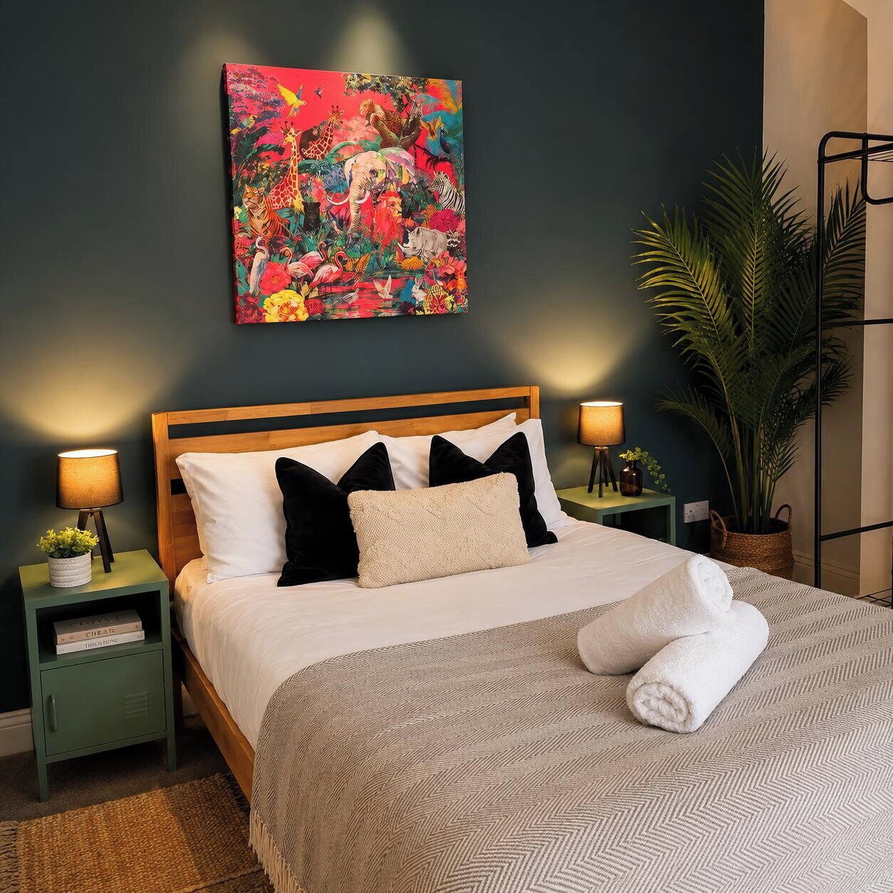 A neatly made bed with a patterned bedspread and pillows, flanked by two bedside tables with lamps and books. A colorful abstract painting adorns the wall above the bed.