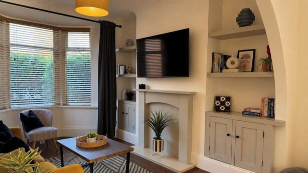 A living room with a fireplace, a television, and a bookshelf. - 3BR Gateshead Home | Free Parking & WiFi (Gateshead)