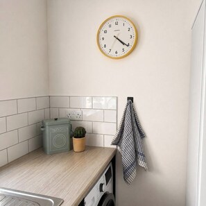 A laundry room with a washing machine, a dryer, a clock, and a small potted plant. - 3BR Gateshead Home | Free Parking & WiFi (Gateshead)