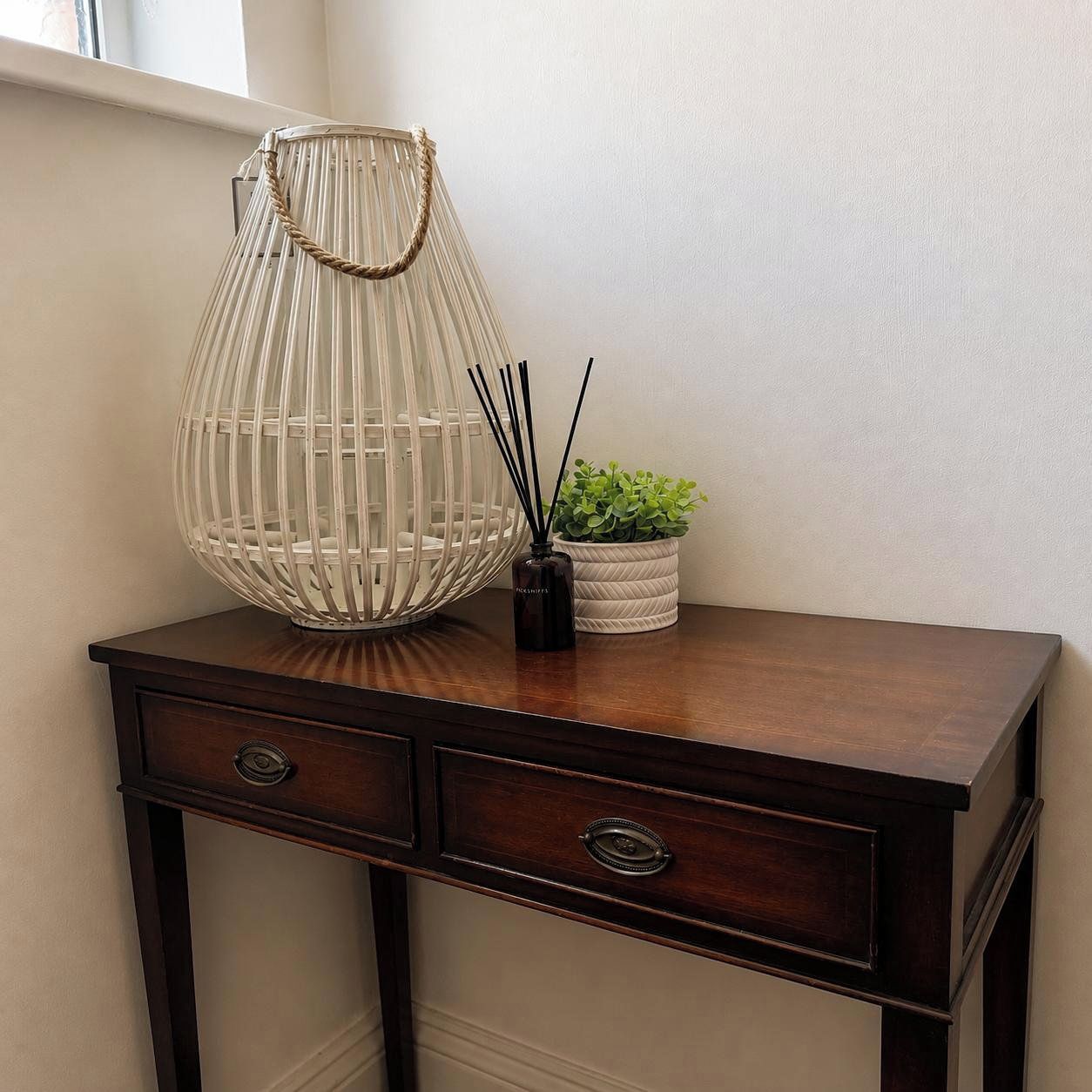 Un bureau en bois avec deux tiroirs et un vase blanc contenant des plantes vertes.