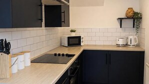 A modern kitchen with a black countertop, white tiles, a microwave, a kettle, and a plant. - 3BR Gateshead Home | Free Parking & WiFi (Gateshead)