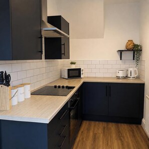 Uma cozinha moderna com bancada preta, azulejos brancos, micro-ondas, chaleira e uma planta.