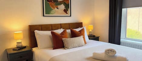 Habitación de hotel con cama, mesita de noche, lámpara, un cuadro en la pared y una ventana con cortinas.