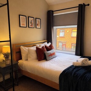 A hotel room with a bed, a nightstand, a window with curtains, and wall art. - 3BR Gateshead Home | Free Parking & WiFi (Gateshead)