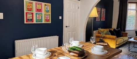 A dining area with a wooden table set for four, a white door, and a dark blue wall with vintage can posters.