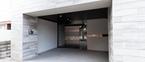 Une entrée moderne avec une porte en verre, un panneau indiquant qu’il est interdit de fumer et une plaque avec le nom au-dessus de la porte.