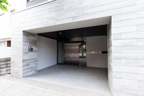 Entrada de um edifício moderno com porta de vidro, placa indicando proibição de fumar e uma placa de identificação acima da porta.