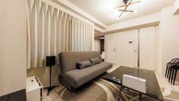 A modern hotel room with a sofa, a desk, a lamp, and a ceiling light fixture.
