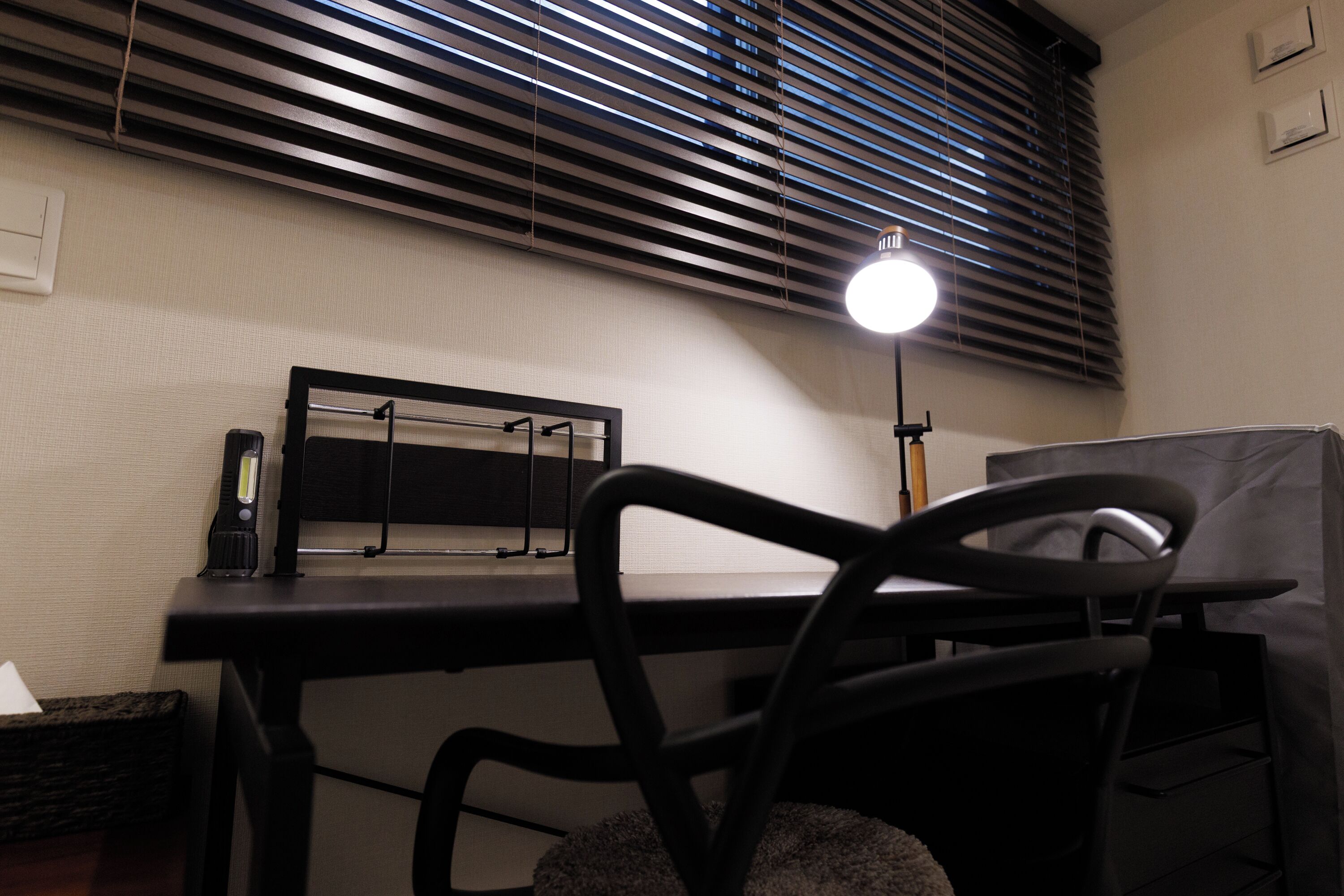 A desk with a lamp, a chair, and a window with blinds.