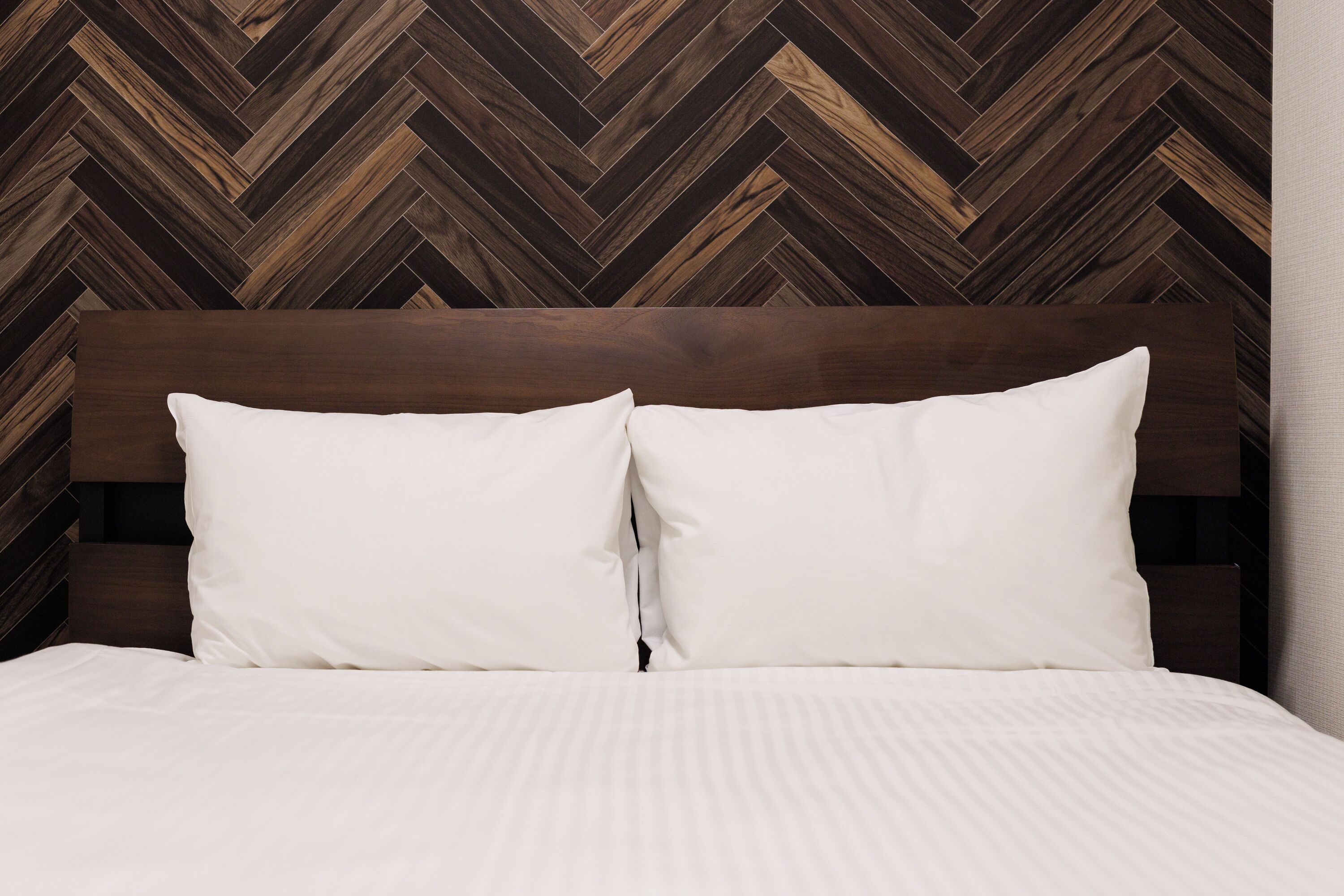Ein Bett mit Holz Kopfteil und weißen Kissen vor einer Wand mit Fischgrätmuster.