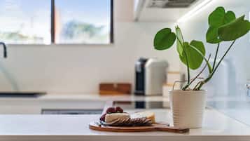 A kitchen counter with a potted plant, a cheese wheel, and a wooden board with sliced bread and grapes.