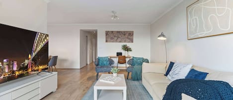 Un salon moderne doté d’un téléviseur à écran plat, d’un canapé, d’une table basse et offrant une vue sur le paysage urbain.