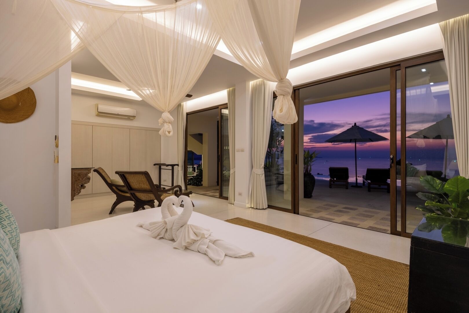 Une chambre d’hôtel avec un grand lit, une vue sur la mer et un balcon avec des sièges pour profiter de l’extérieur.