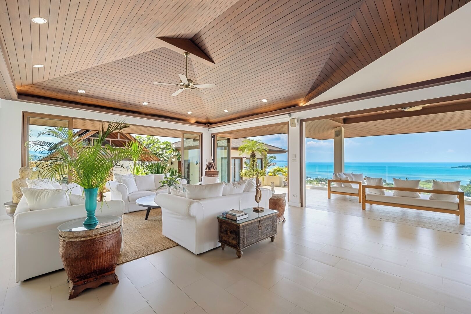 A spacious living area with a ceiling fan, white sofas, a coffee table, and a view of the ocean.