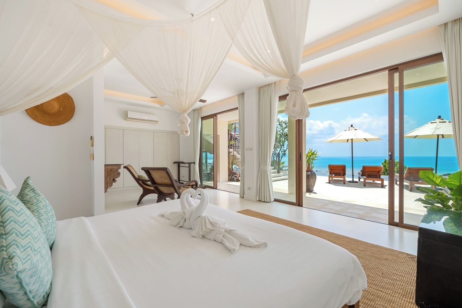 Une chambre d’hôtel avec un grand lit, une vue sur l’océan et un balcon avec des sièges pour profiter de l’extérieur.