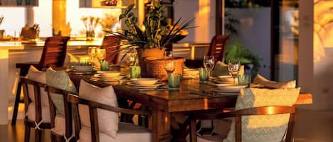 A dining area with a wooden table set for four, surrounded by chairs with white cushions.