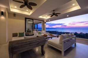 Ein modernes Wohnzimmer mit Essbereich, großen Fenstern und Blick auf das Meer bei Sonnenuntergang.
