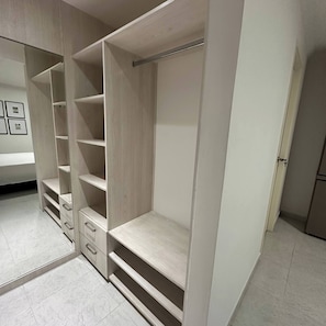 Un vestidor con amplios estantes y cajones, un espejo de cuerpo entero y una puerta que da a otra habitación.
