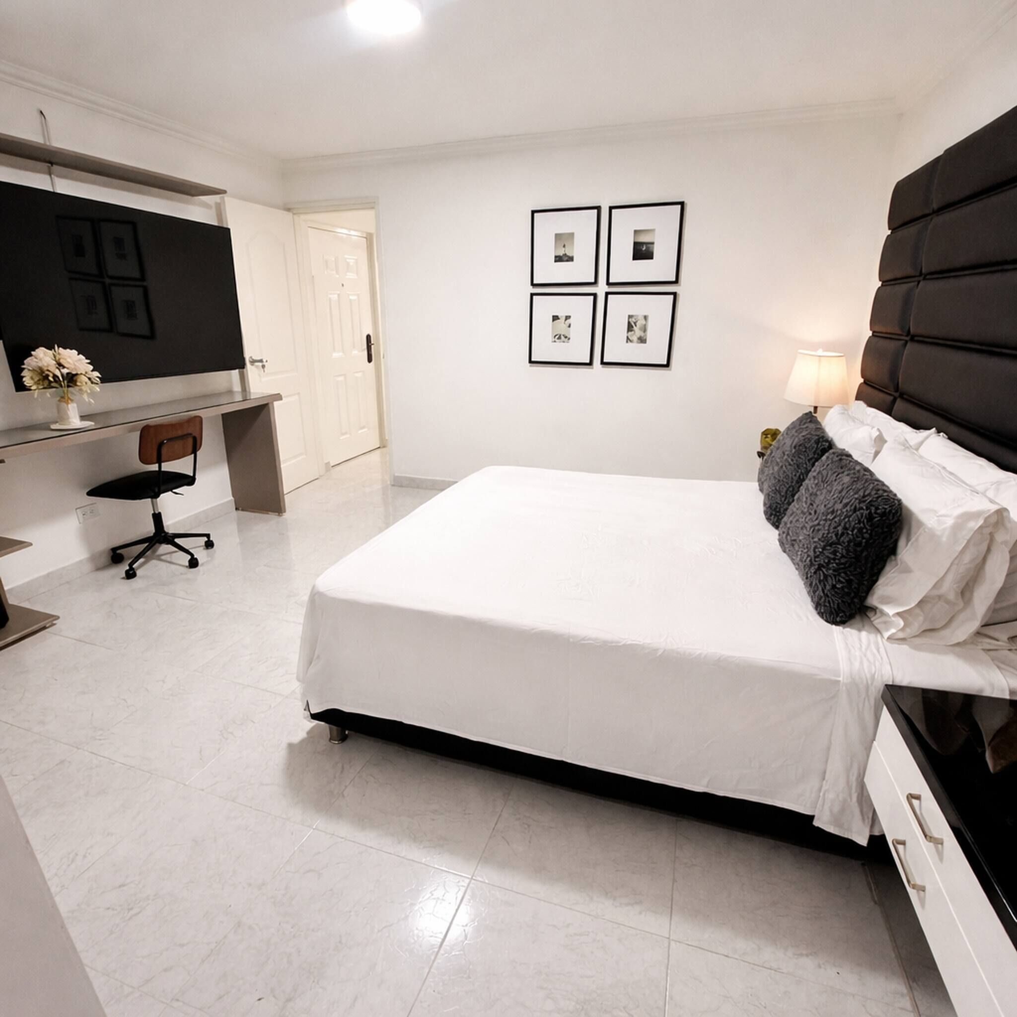 Ein Hotelzimmer mit einem Bett, einem Schreibtisch, einem Sessel, einem Fernseher und gerahmten Bildern an der Wand.