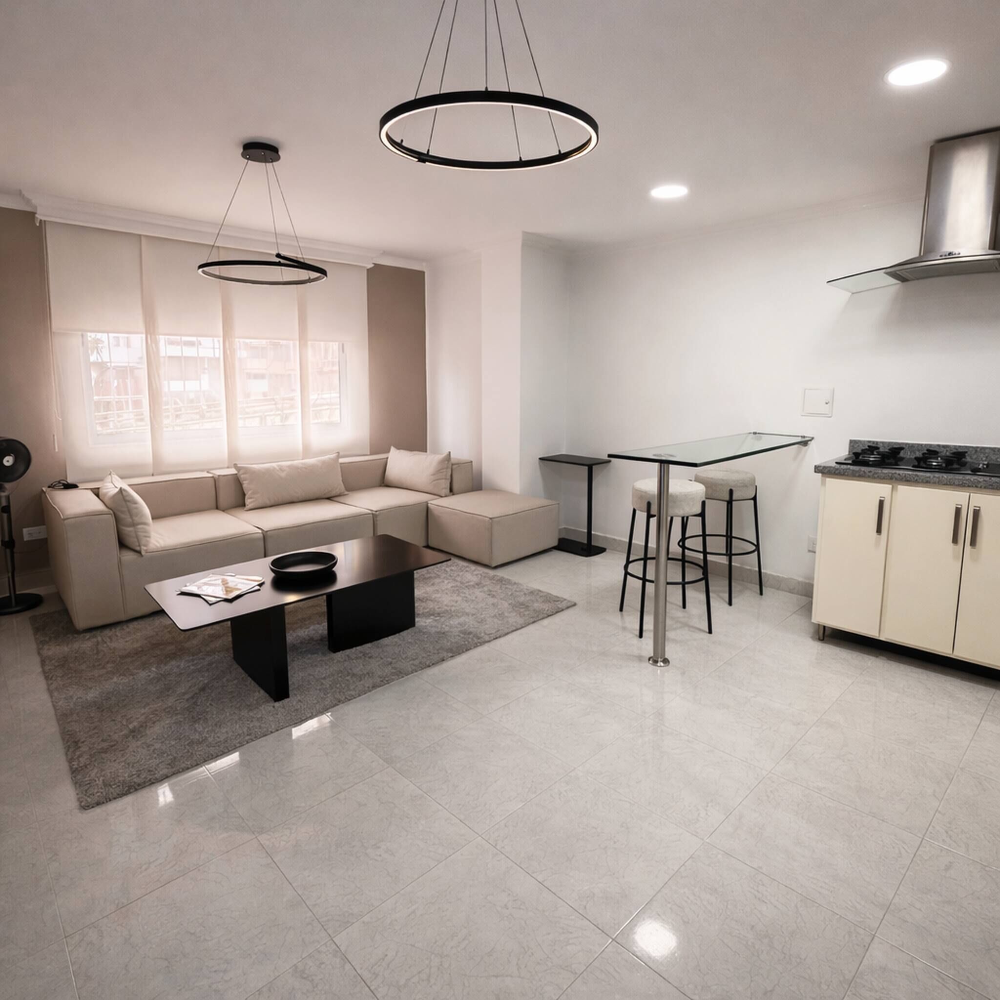 A modern living room with a sectional sofa, a coffee table, and a dining area with a glass table and bar stools.