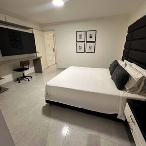 Un dormitorio con cama, una silla, un escritorio y una puerta.