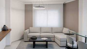 Een moderne woonkamer met een hoekbank, een salontafel met glazen blad en een hanglamp.