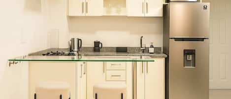 A compact kitchen with a built-in oven, a refrigerator, and a glass-top island with two stools.