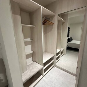 Un vestidor amplio con estantes abiertos, una barra para colgar ropa y una puerta con espejo.