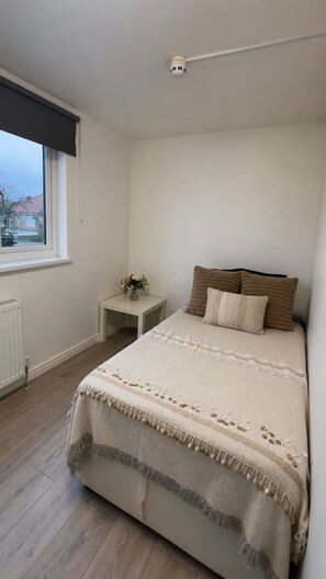 Ein Schlafzimmer mit einem Bett, einem Nachttisch, einem Fenster und einer Deckenleuchte.