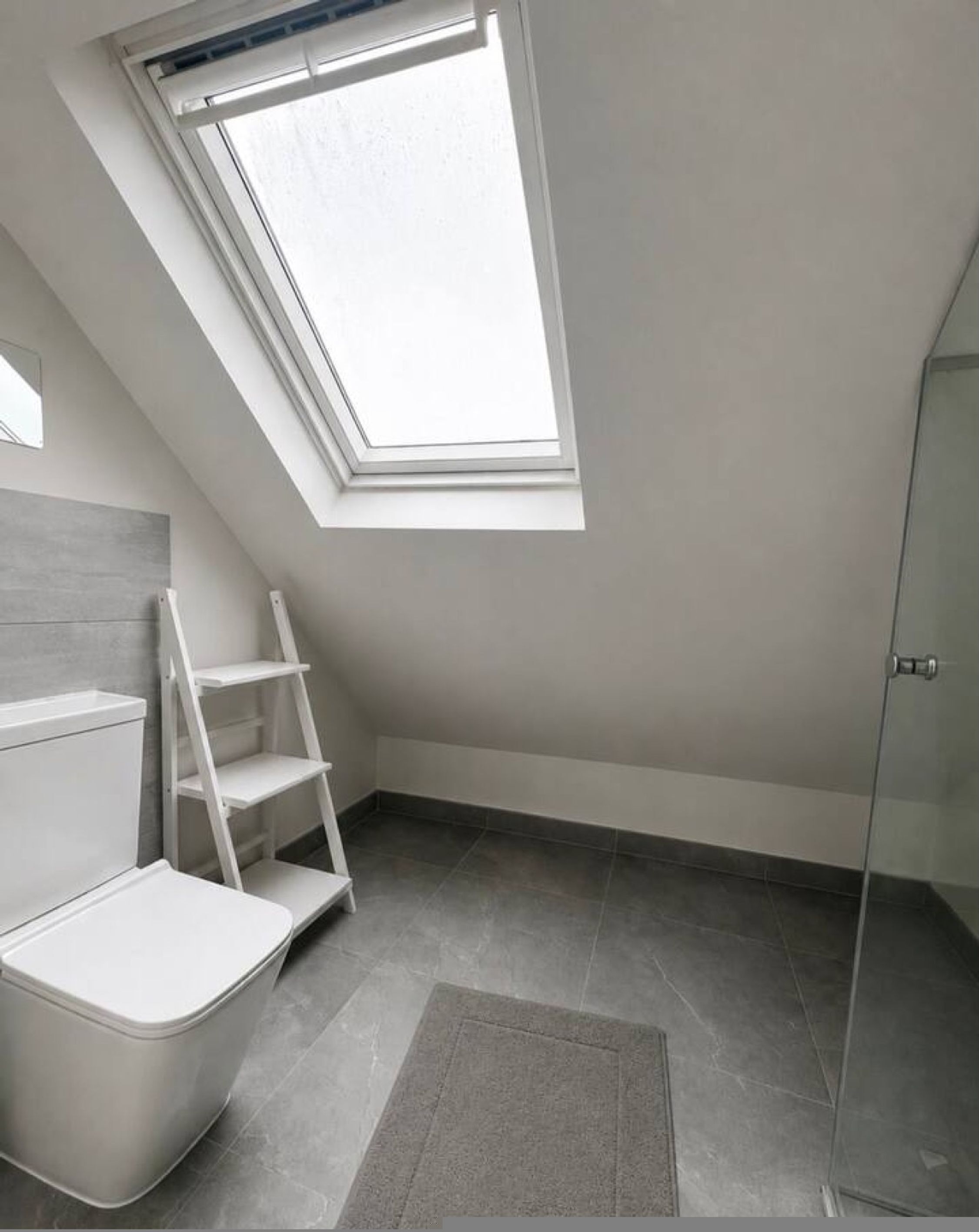 A small, modern bathroom with a skylight, a shower, and a white vanity.