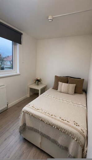Ein Schlafzimmer mit Bett, Nachttisch, Fenster und Deckenleuchte.