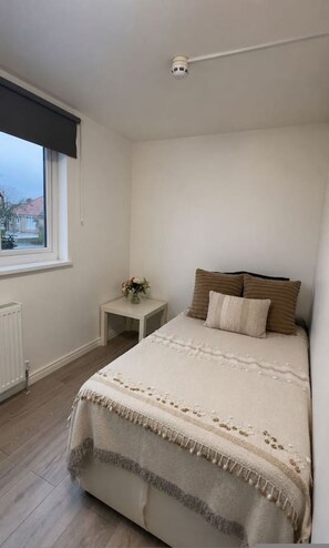 Ein Schlafzimmer mit Bett, Nachttisch, Fenster und Deckenleuchte.