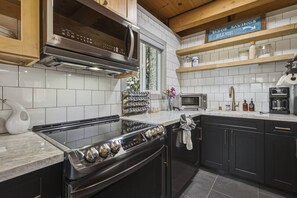 Cocina moderna con estufa de acero inoxidable, microondas y cafetera. Hay armarios de madera y un cartel sobre la encimera.