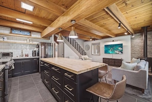A modern kitchen with a central island, dark cabinetry, and a wooden ceiling. - Fir Sure Chalet - Dog friendly modern cabin in SLT (South Lake Tahoe)