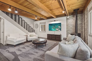 A modern living room with a staircase, a fireplace, and a large TV. - Fir Sure Chalet - Dog friendly modern cabin in SLT (South Lake Tahoe)