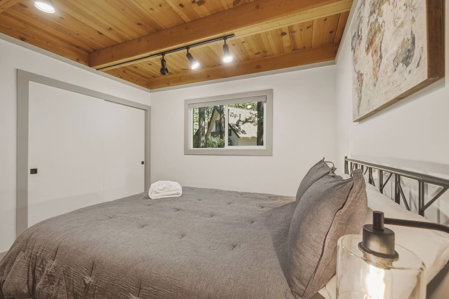 A bedroom with a bed, a window with a view, and a painting on the wall.