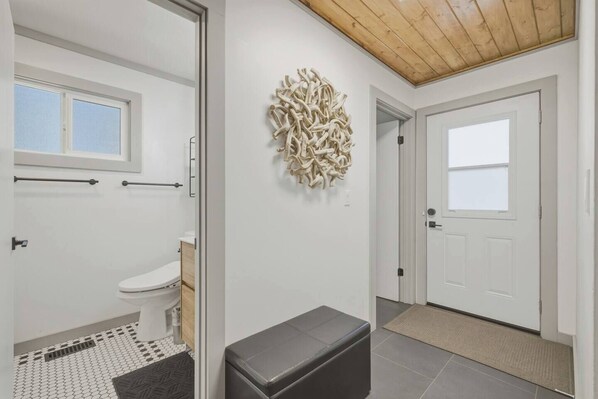 A modern bathroom with a toilet, bidet, and a shower area. There is a bench in the hallway and a decorative wall piece. - Fir Sure Chalet - Dog friendly modern cabin in SLT (South Lake Tahoe)