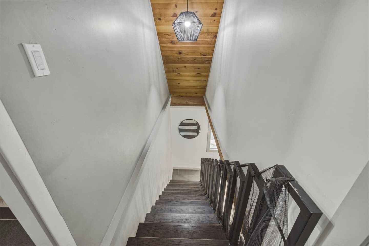 Un escalier avec des marches en bois et des rampes en métal, menant à une pièce dotée d’une fenêtre circulaire.