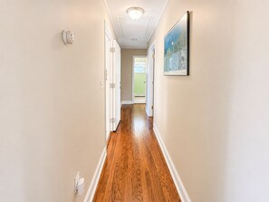 A hallway with wooden flooring, white walls, and a ceiling light. - Beach Getaway 3BR • Parking • Beach Badges (Seaside Heights)