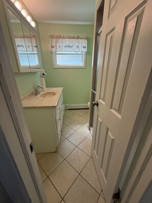 Une salle de bain avec un meuble-lavabo, un évier, un miroir et une fenêtre avec des rideaux.
