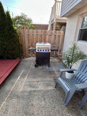 An outdoor barbecue grill with a wooden fence and a potted plant in the background. - Beach Getaway 3BR • Parking • Beach Badges (Seaside Heights)