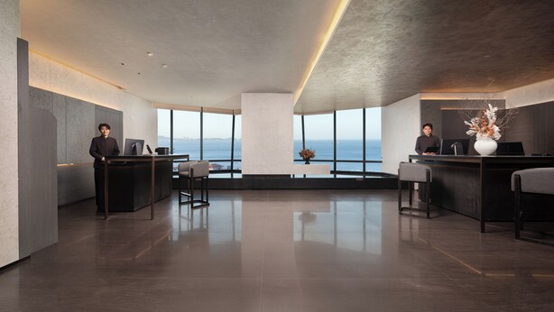 A modern hotel lobby with a reception desk, seating area, and large windows offering a view of the sea. - Yantai First Beach Seaview Yaduo Hotel (Yantai)