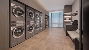 A modern laundry facility with multiple washing machines, a wooden floor, and a view of a building through large windows. - Yantai First Beach Seaview Yaduo Hotel (Yantai)