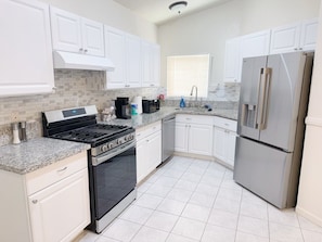 A kitchen with white cabinets, a stainless steel refrigerator, a stove, and a microwave. - Modern 3BR Single-Story Home with Spacious Yard (North Las Vegas)