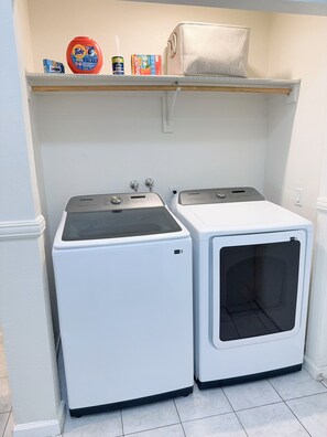 A laundry area with two front-loading washing machines and a shelf above containing laundry supplies. - Modern 3BR Single-Story Home with Spacious Yard (North Las Vegas)