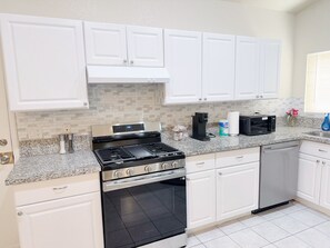 Cocina con gabinetes blancos, estufa de acero inoxidable, lavavajillas y microondas.
