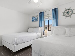 Ein Hotelzimmer mit zwei Betten, einem Deckenventilator, einer Schiffslenken-Dekoration und einem Fenster mit Vorhängen.