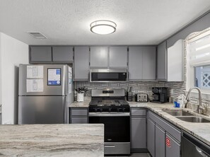 A modern kitchen with stainless steel appliances, a microwave, a stove, and a built-in oven. - Coconut Cottage! Golf Cart Friendly Community! (Panama City Beach)